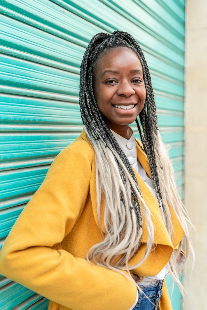 portrait of a smiling african american woman with braids wearing yellow coat